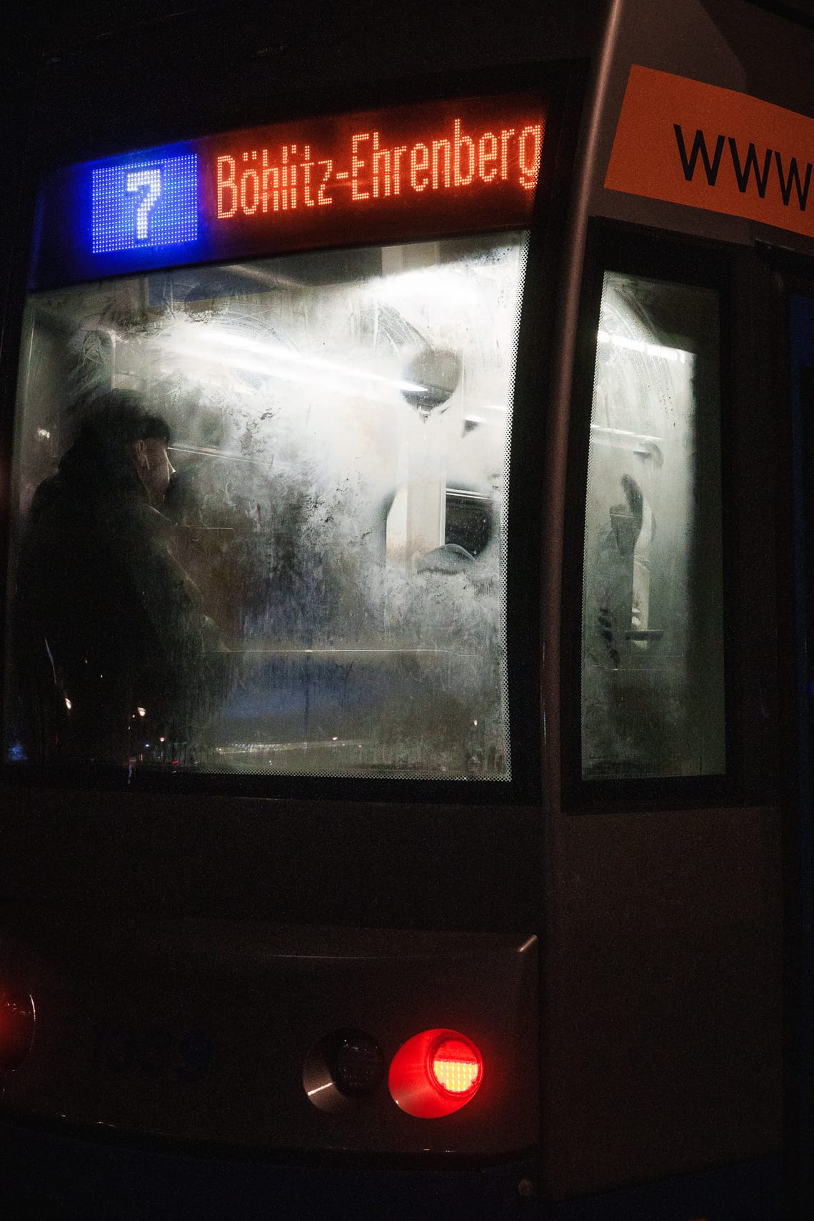 Eine Person hinter einer beschlagenen Scheibe der an der Haltestelle wartenden Tram.